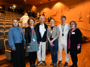 Bilde av seks personer som står i et stort auditorium. 